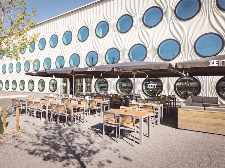 Aussenbereich eines Cafés mit runden Fenstern an der modernen Fassade.