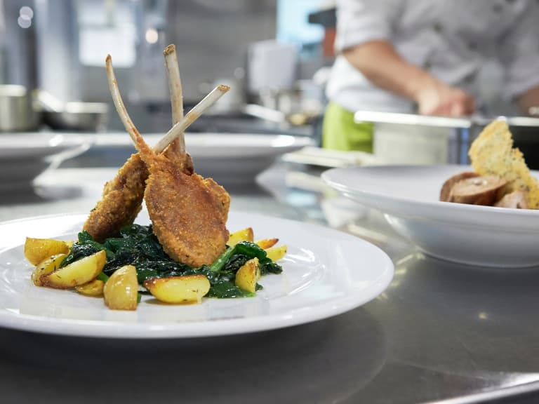 Gericht mit Lammkoteletts und Kartoffeln auf Teller in Küche.