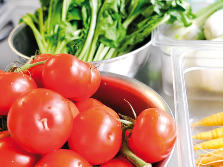 Schüssel mit Tomaten, Gemüse im Hintergrund."  