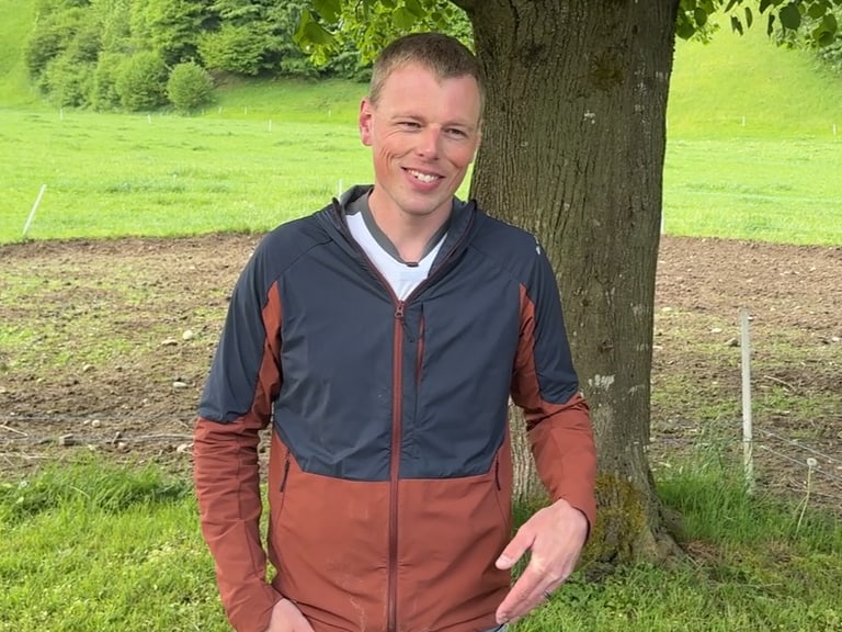 Person steht entspannt vor einem Baum auf Wiese.