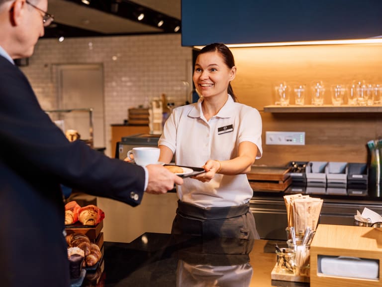 Kellnerin überreicht Teller an Kunden an der Theke eines Cafés.