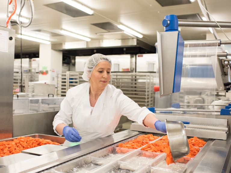 Arbeiterin in der Fabrik verarbeitet Karotten an der Produktionslinie.
