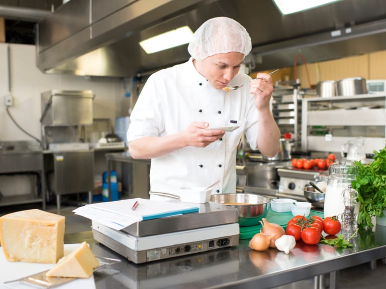 Koch probiert Suppe in der Grossküche.