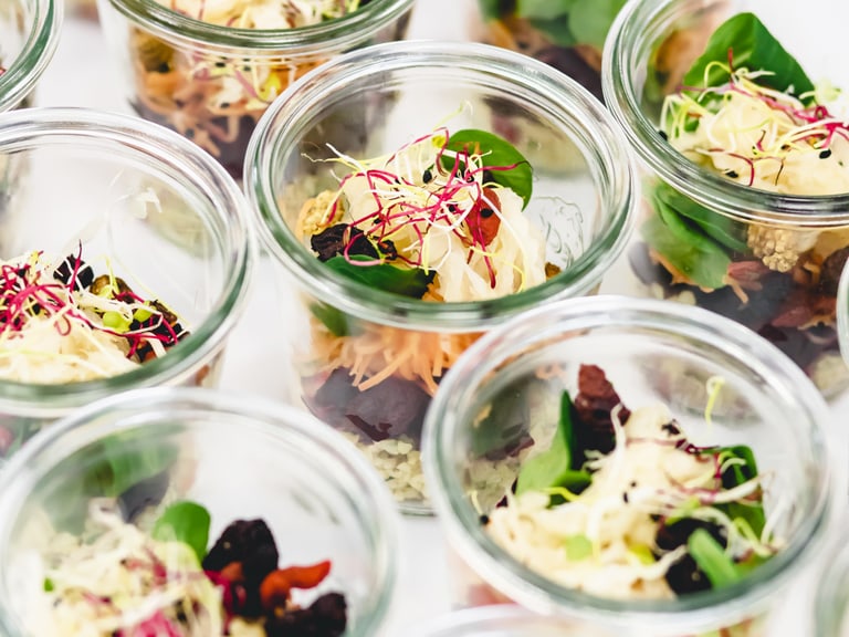 Mehrere Gläser mit Salat und Sprossen gefüllt.