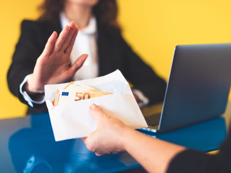 Person lehnt Umschlag mit Geld vor Laptop ab.