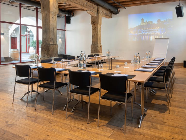 Konferenzraum mit Holzboden und Projektionsfläche.