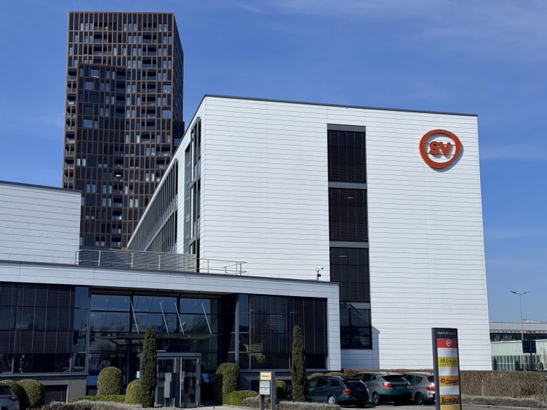 Weisses Gebäude mit SV-Logo und modernem Turm im Hintergrund.
