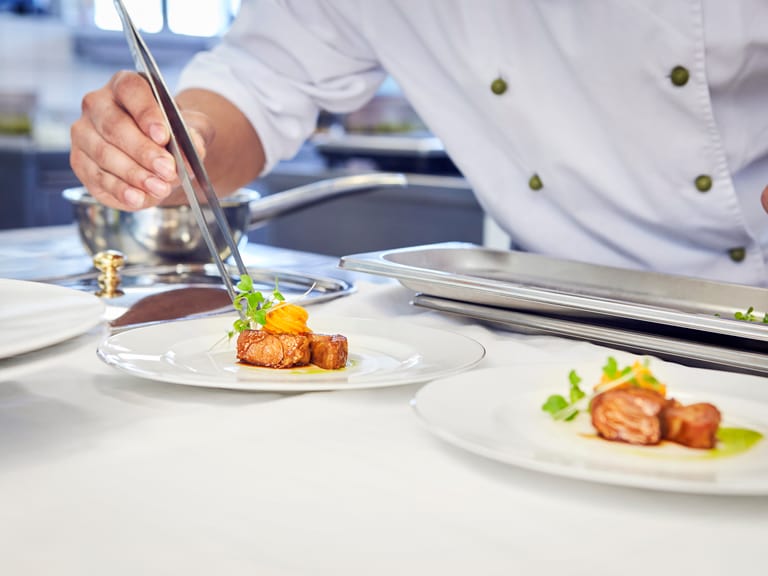 Koch arrangiert Gourmetgericht auf Teller in Küche.