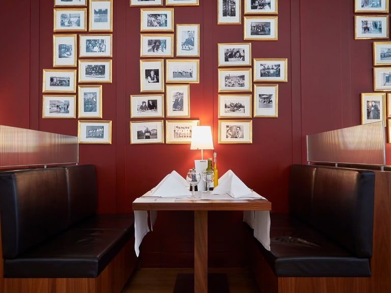 Restaurantkabine mit gerahmten Fotos an roter Wand.