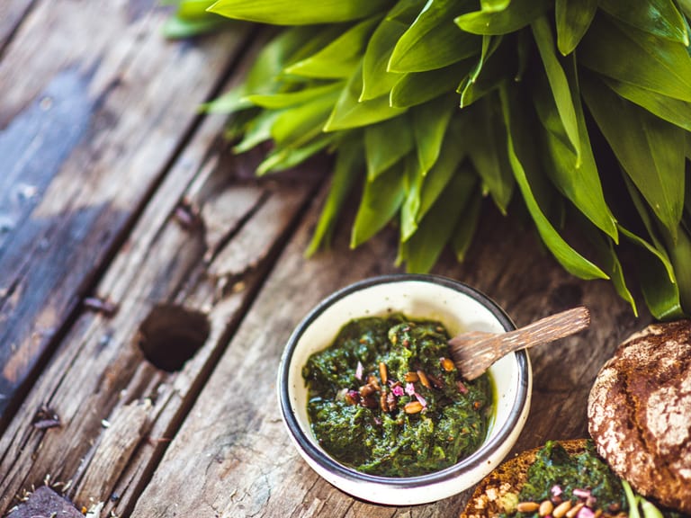Bärlauchpesto mit frischen Blättern auf Holzuntergrund.