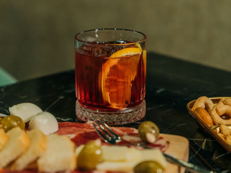 Campari-Cocktail mit Orangen auf Tisch mit Snacks.
