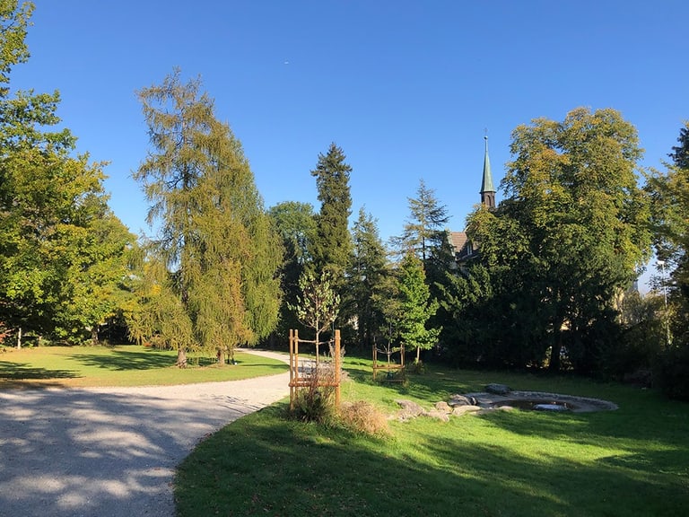 Parklandschaft mit Kirche im Hintergrund unter blauem Himmel.