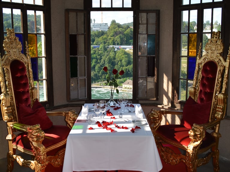 Eleganter Tisch mit Rosenblättern und goldenen Stühlen in Fensterraum.
