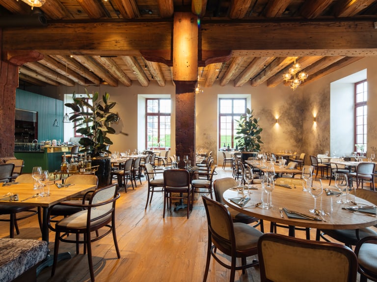 Elegantes Restaurant mit Holzbalkendecke und runden Tischen.