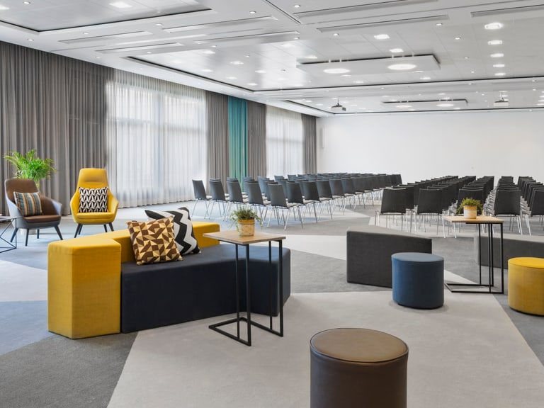 Konferenzraum mit Sitzreihen und Sofas.