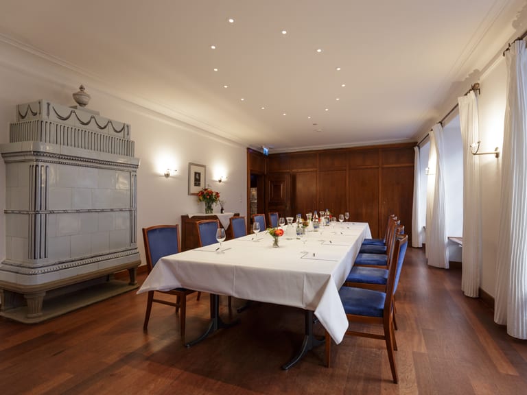 Eleganter Speiseraum mit Tisch, blauen Stühlen und Kachelofen.