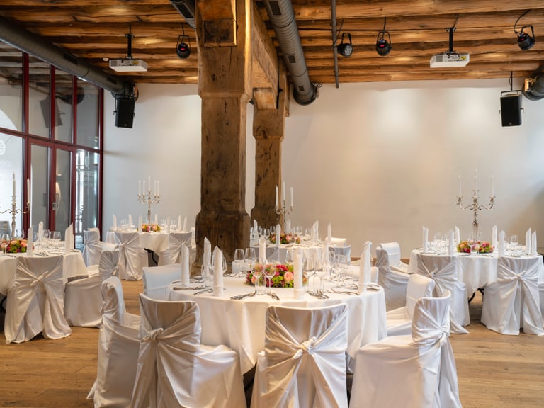 Eleganter Bankettsaal mit weissen Tischdecken und Kerzenhaltern.