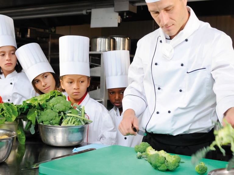 Koch zeigt Kindern das Zubereiten von Gemüse in der Küche.