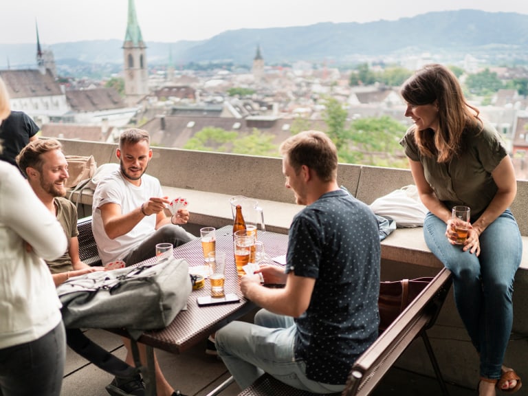 Gruppe von Freunden auf Terrasse mit Stadtblick im Hintergrund.