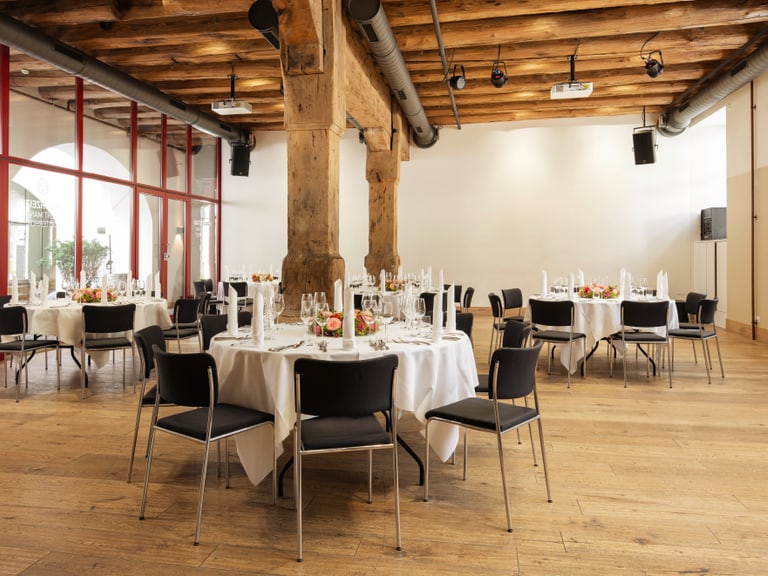 Elegant gedeckter Raum mit runden Tischen und Holzbalkendecke.