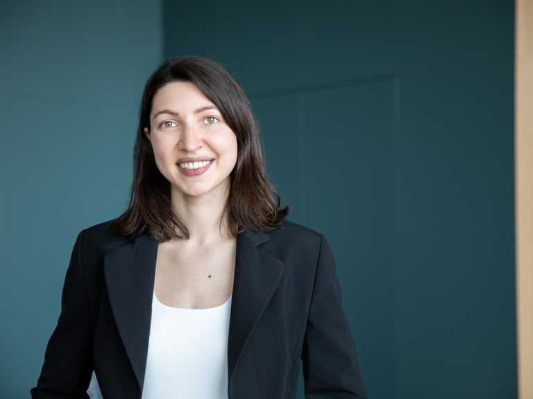 Frau in schwarzem Blazer vor blauem Hintergrund.