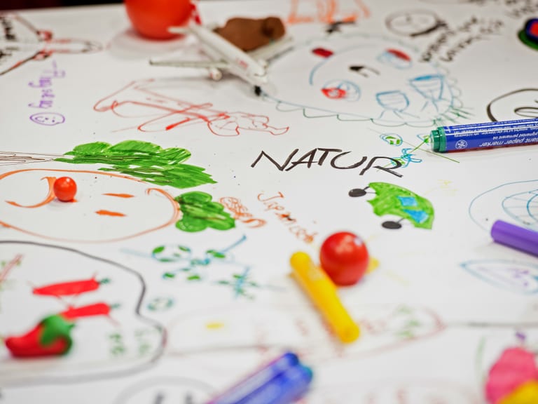 Kreative Zeichnungen und Spielzeug auf Tisch, 'NATUR' geschrieben.