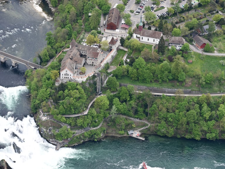 Luftbild des Rheinfalls mit Schloss Laufen und Gebäuden in grüner Landschaft.