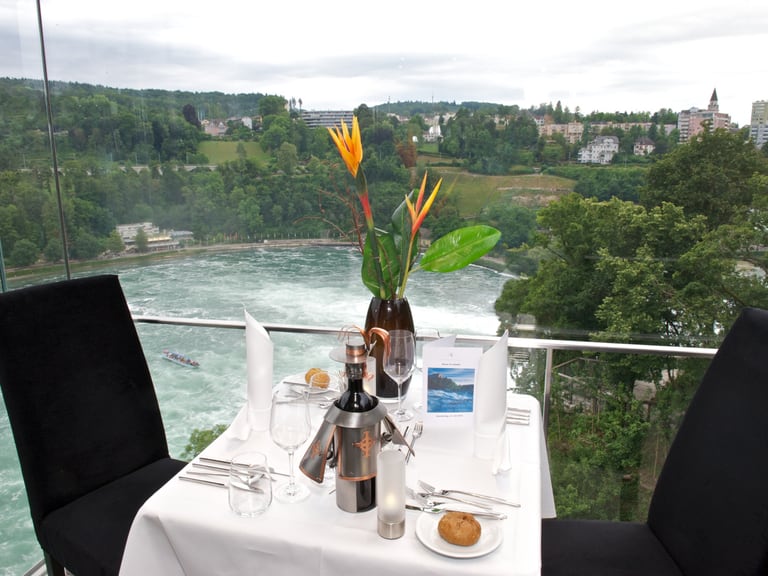 Tischgedeck mit Blick auf den Fluss und grüne Landschaft.",