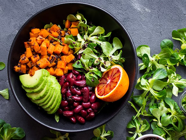 Schüssel mit Gemüse, roten Bohnen und halber Orange auf grauem Hintergrund.