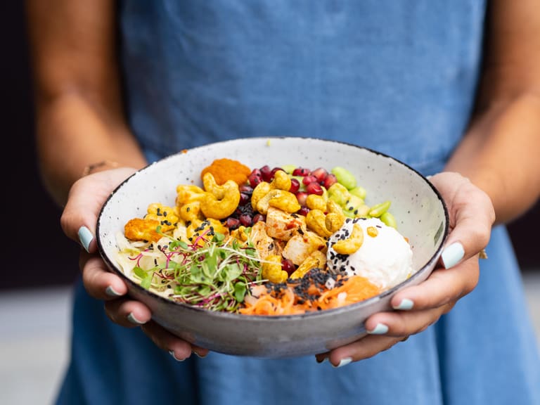Person hält eine Schüssel mit buntem vegetarischen Essen.