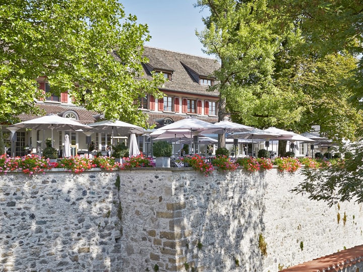 Gemütliches Café mit Terrasse an Steinmauer mit Blumen und Bäumen.