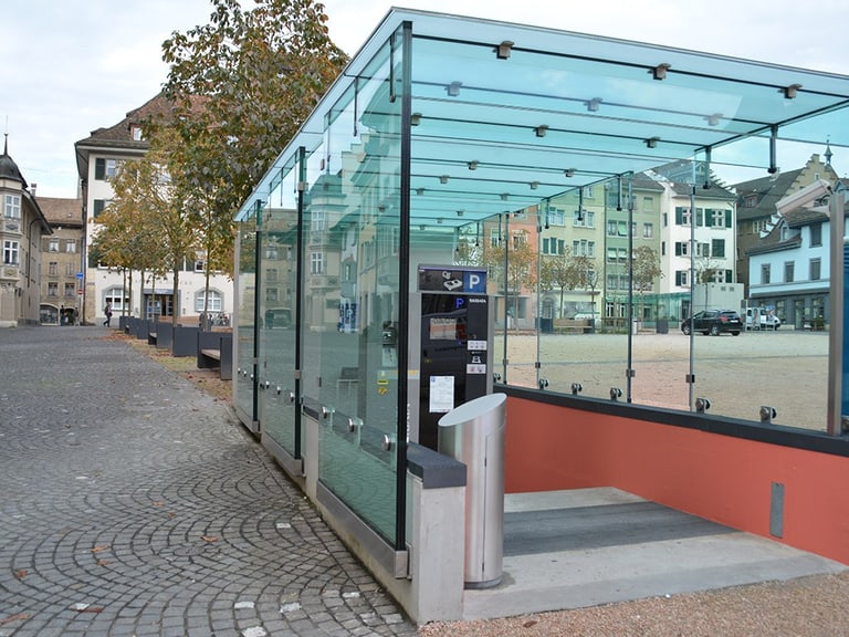 Glasüberdachung mit Parkscheinautomat in städtischem Platz.