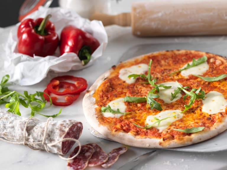 Pizza auf Marmor mit Peperoni, Salami und Nudelholz.