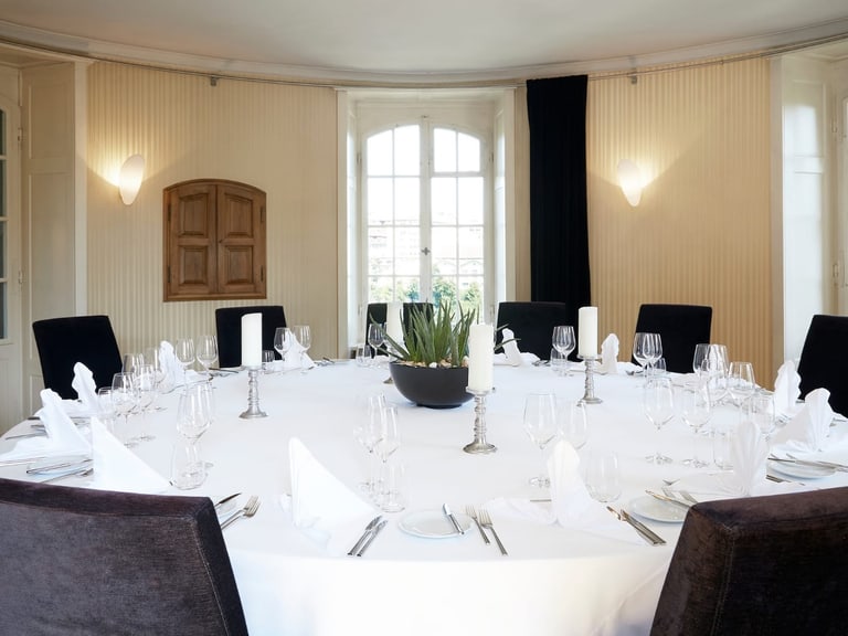 Rund gedeckter Esstisch in elegantem Raum mit Kerzen.",