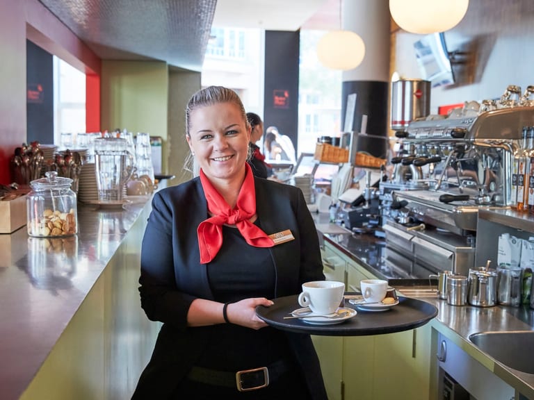 Kellnerin mit Tablett in einem Café mit Espressomaschine.
