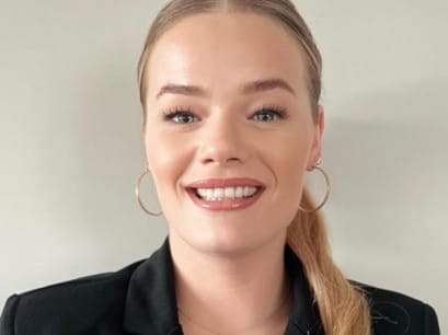 Porträt einer lächelnden Frau mit Pferdeschwanz und Ohrringen.