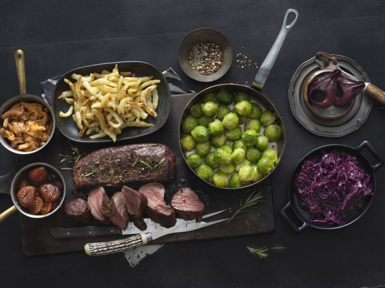 Ein hergerichtetes Tisch mit verschiedenen Gerichten, einschliesslich Fleisch, Rosenkohl und Rotkohl.