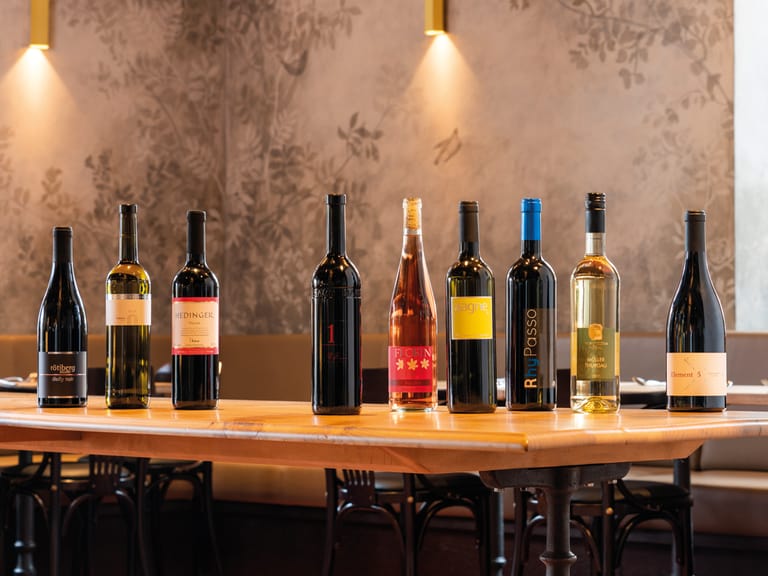 Acht Weinflaschen auf einem Holztisch in einem Restaurant.