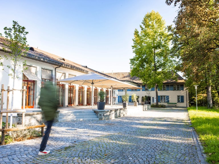 Person walking past a sunny building with a terrace.