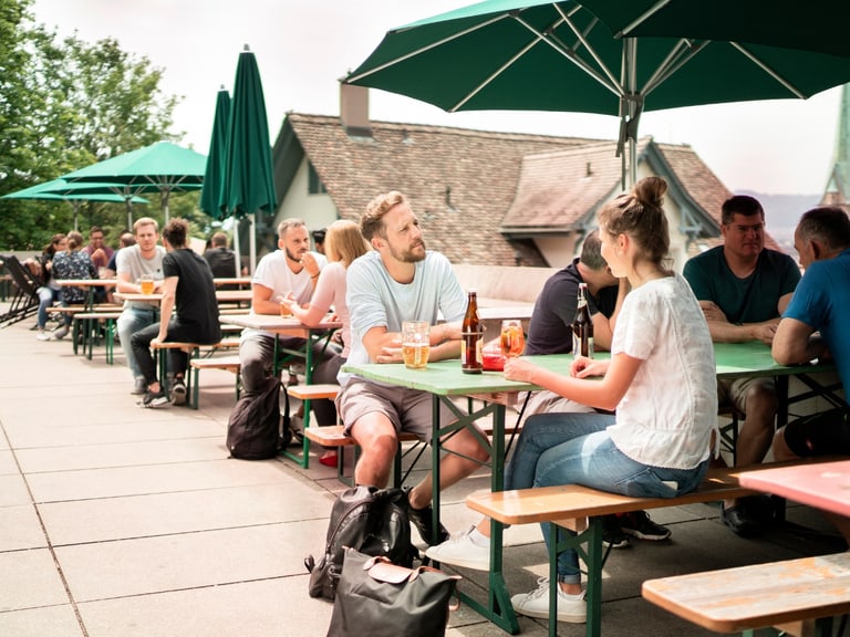 Menschen sitzen an Tischen im Freien mit Sonnenschirmen.",