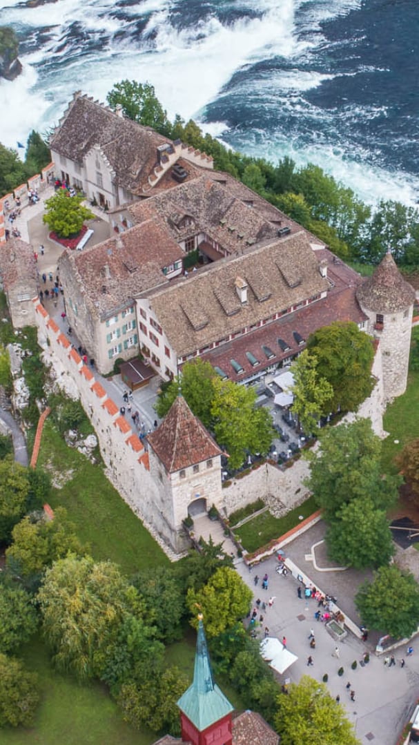 Luftbild eines Schlosses am Fluss mit Wasserfällen und einer Brücke.