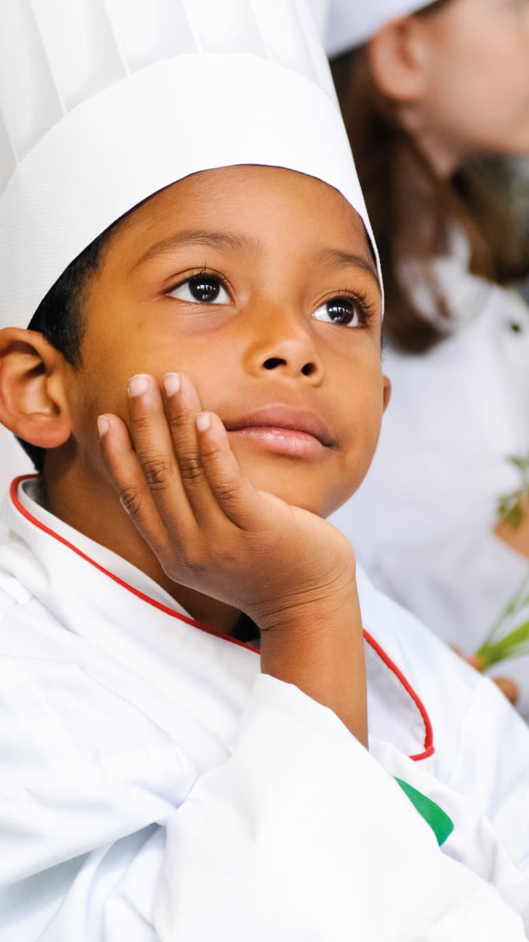 Junges Kind im Kochoutfit schaut nachdenklich zur Seite.