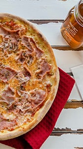 Pizza mit Schinken und Glas Eistee auf Tisch.