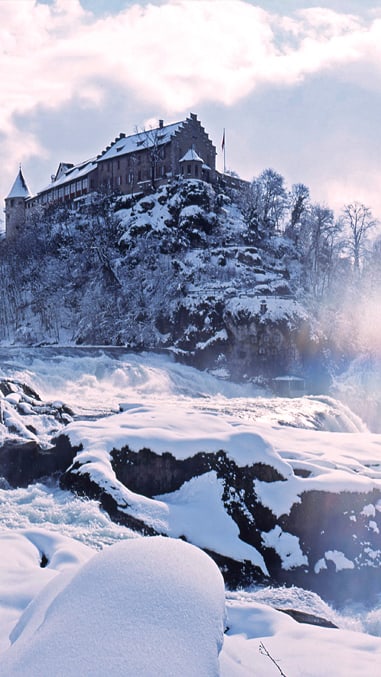 Schloss und Flusslandschaft im Schnee bei Sonnenuntergang.