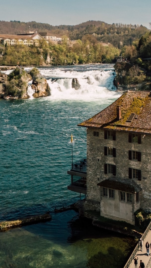 Blick auf das Rheinfall-Gebiet mit Wasserfall und Gebäude am Ufer.