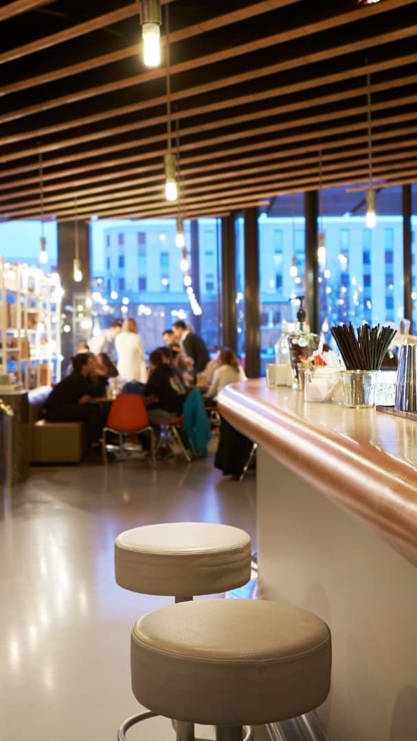 Moderne Bar mit langen Tresen, Sitzhockern und grossen Fenstern bei Abenddämmerung.