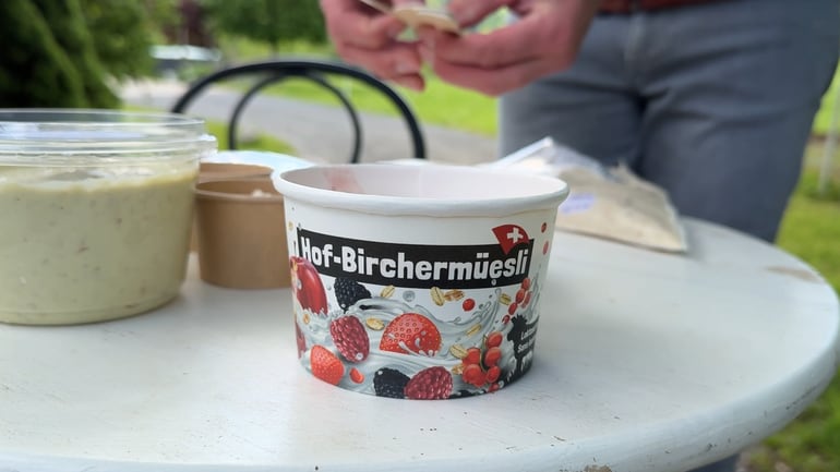 Tisch mit Becher Hof-Birchermüesli im Freien.
